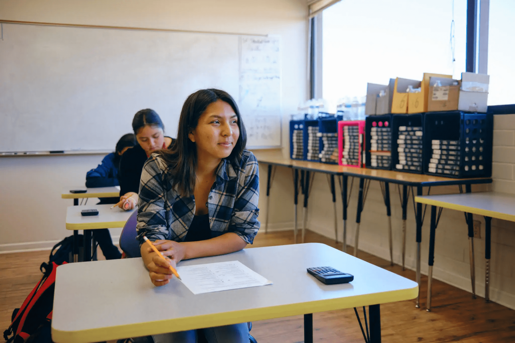 Student in classroom with desk and papers.
