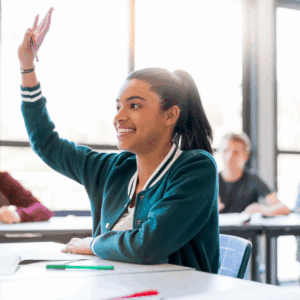 Student raising hand in classroom, smiling.