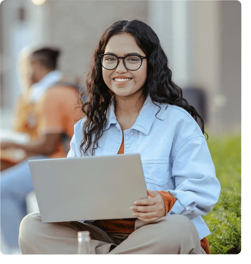 Smiling person with laptop sitting outside.
