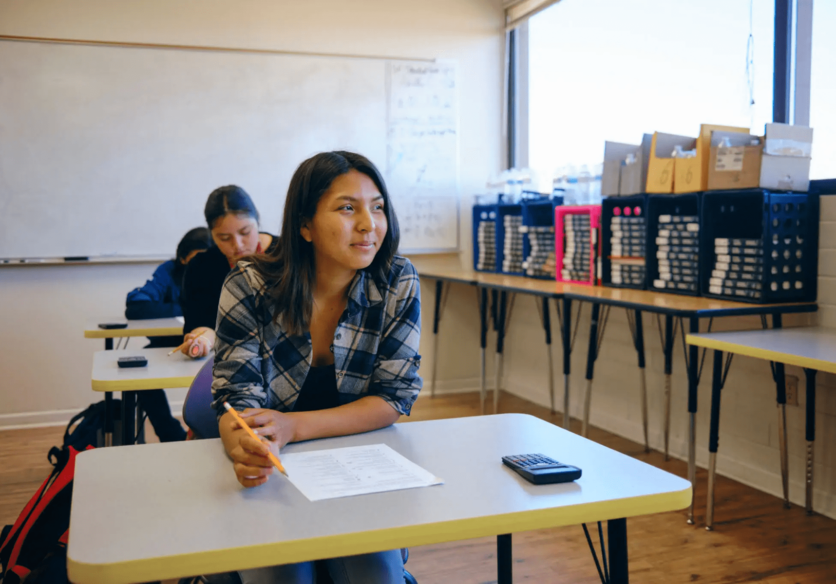 Student in classroom with desk and papers.